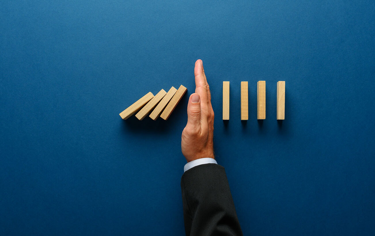 Top,View,Of,Businessman,Hand,Stopping,Falling,Dominos,In,A Top view of businessman hand stopping falling dominos in a business crisis management conceptual image.